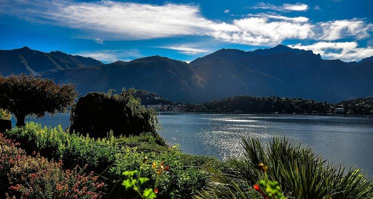 Paysage serein au bord du lac avec montagnes et jardins colorés.