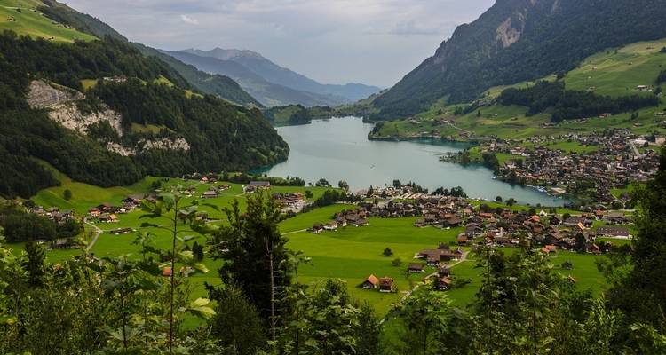 Une vue sereine de vallée avec un lac, des montagnes et des maisons dispersées.