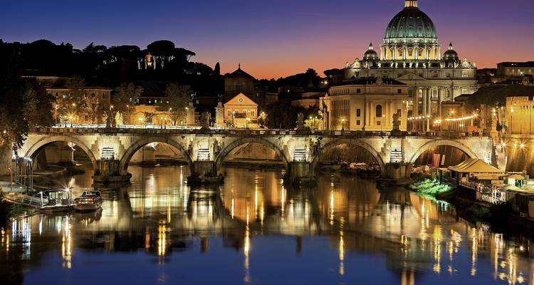 Cité du Vatican la nuit avec la basilique Saint-Pierre illuminée et un pont sur le fleuve.