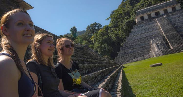 Tres viajeros descansan en escalones de piedra frente a la Pirámide de las Inscripciones escalonada en Palenque.