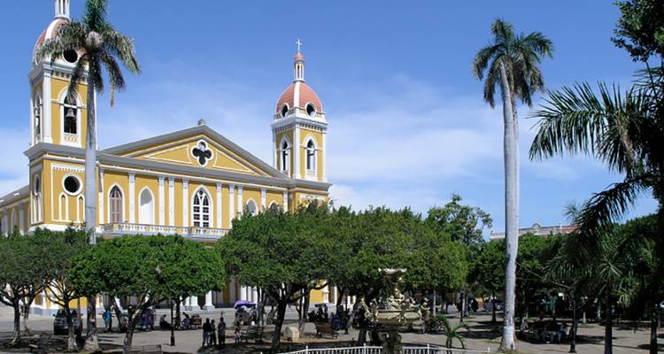La amarilla Catedral de Granada se eleva sobre un parque arbolado de palmeras bajo un cielo azul claro nicaragüeño.