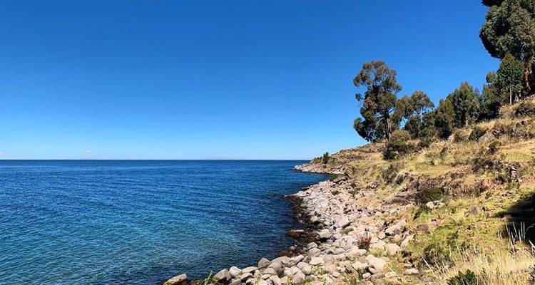 Rivage rocheux et eaux bleu profond du lac Titicaca sous un ciel azur dégagé.
