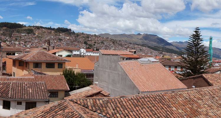 Vue panoramique sur les toits en terre cuite de Cusco avec les montagnes des Andes au loin.
