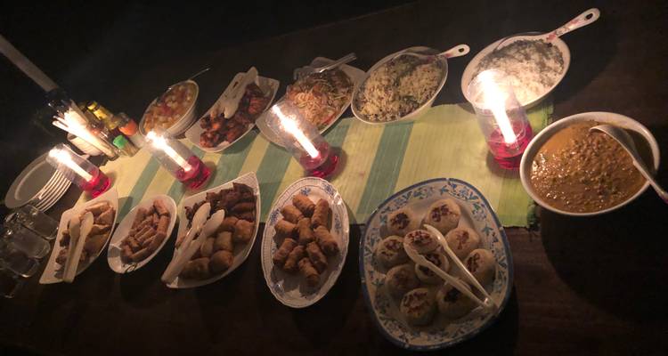 Buffet dînatoire aux chandelles présentant diverses spécialités maloudiennes sur une table en bois la nuit.