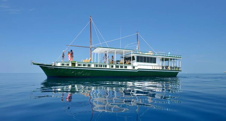 Bateau de croisière classique vert maldivien se reflétant parfaitement dans la mer tropicale immobile sous un ciel sans nuages.