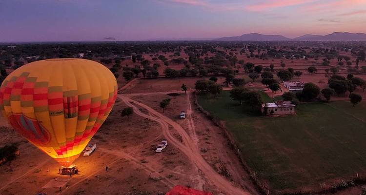 Un ballon à air chaud illuminé se gonfle dans la campagne ouverte au crépuscule avec un ciel rose et violet.