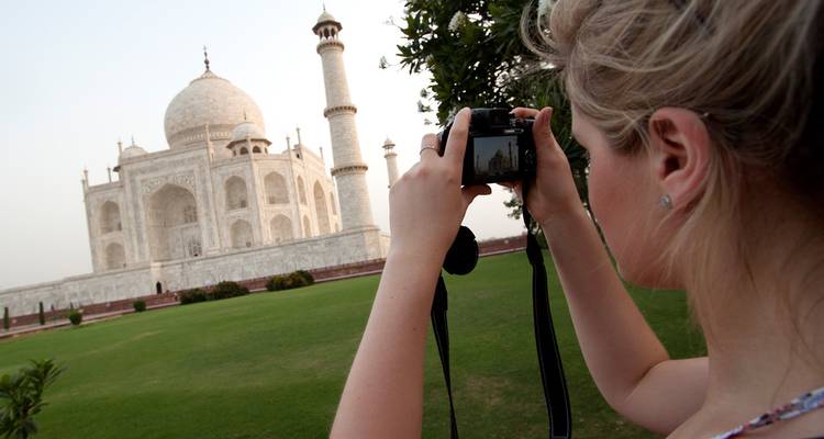 Voyageur photographiant le Taj Mahal depuis des pelouses verdoyantes luxuriantes sous une lumière douce de l'après-midi.