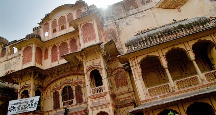 Demeure historique rajasthane aux balcons ornementés, avec un reflet du soleil qui transparaît au-dessus du toit carrelé.