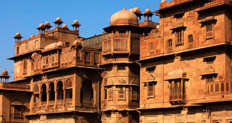 Palacio de arenisca iluminado por el sol con balcones intrincados y ventanas de celosía contra un cielo azul despejado.