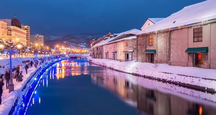 Canal d'Otaru bordé de neige illuminé de lumières bleues et entrepôts historiques au crépuscule.