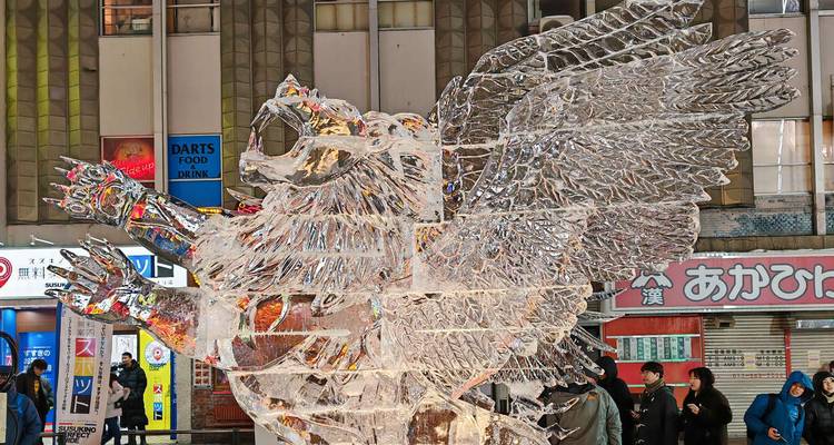 Sculpture de glace complexe d'une créature ailée exposée sur une rue commerçante animée.