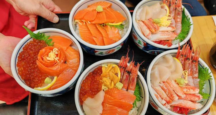 Cinq bols de riz aux fruits de mer colorés garnis de saumon, œufs de poisson, crevettes et oursin disposés sur un plateau.