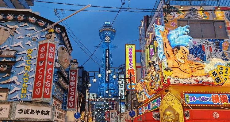 Rue de divertissement brillamment illuminée avec des enseignes au néon menant vers la tour Tsutenkaku bleue.