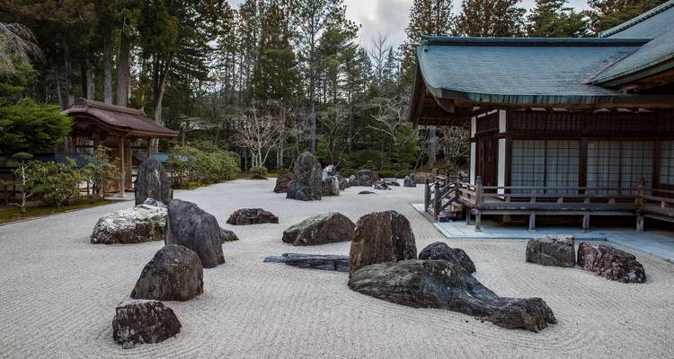 A serene dry rock garden with large dark stones beside traditional wooden temple buildings.
