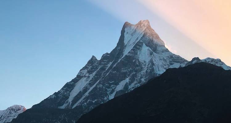 Distinctive Machapuchare peak catches first light with clear blue sky backdrop.