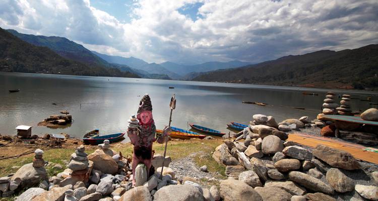 Lago tranquilo rodeado de colinas con botes de madera coloridos y pilas de cairns de piedra en primer plano