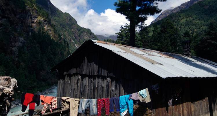 Cabaña rústica de madera con ropa secándose en un tendedero ubicada en un valle himalayo rodeado de bosques