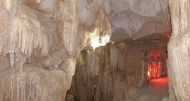 Intérieur d'une grotte calcaire avec des stalactites et un éclairage dramatique illuminant les formations rocheuses.