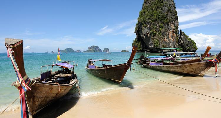 Les bateaux traditionnels à longue queue en bois reposent sur une plage de sable doré avec des îles karstiques en arrière-plan.