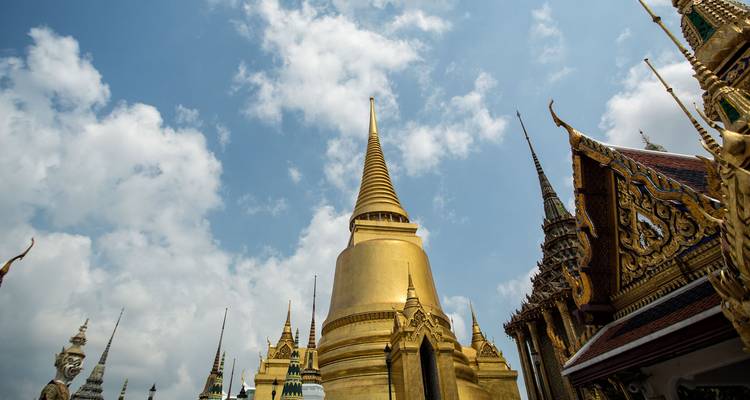 Estupa dorada y elegantes torres de templos del complejo del Gran Palacio de Bangkok extendiéndose hacia un cielo azul.