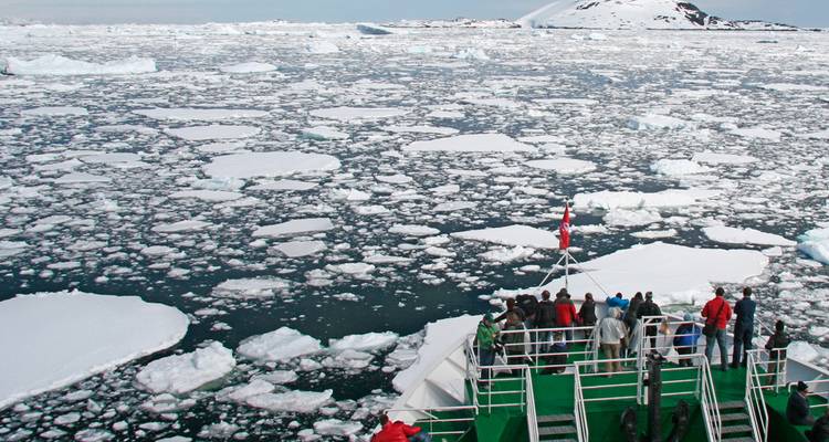 Los pasajeros en la proa del barco observan amplios campos de hielo marino y icebergs adelante
