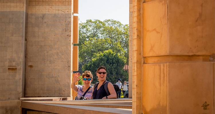 Two women wave from within the astronomical instruments of Jantar Mantar under a clear sky.