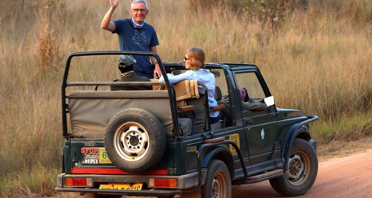 Tourists standing in an open-top jeep on a dirt track during a wildlife safari.