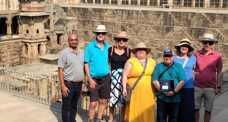 A small tour group poses in front of an ornate stepwell made of carved stone.