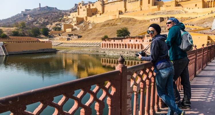 A couple leans on a railing overlooking the reflective lake beside Amber Fort’s ochre walls.