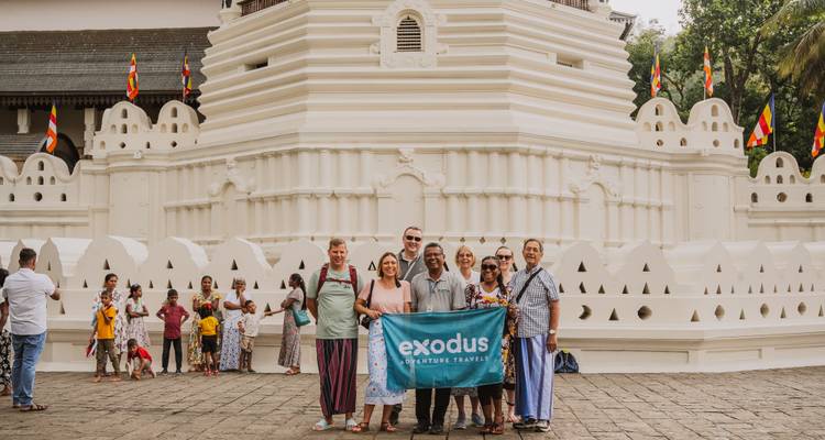 Grupo de tour posando con pancarta afuera del complejo del blanco Templo de la Muela.