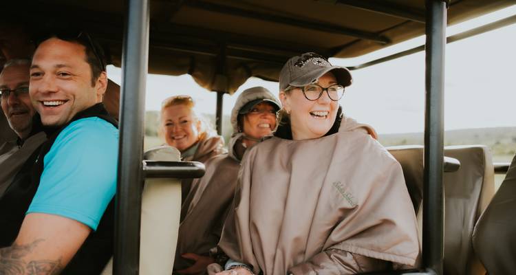 Des touristes heureux portant des ponchos voyageant dans un véhicule de safari ouvert.