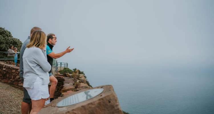 Les visiteurs se tiennent à un point de vue sur une falaise enveloppée de brouillard et font des gestes en direction du vaste océan en contrebas.