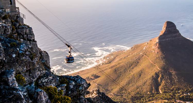 Funiculaire bleu descendant les falaises escarpées de la Montagne de la Table avec la Tête de Lion et la côte atlantique en dessous.