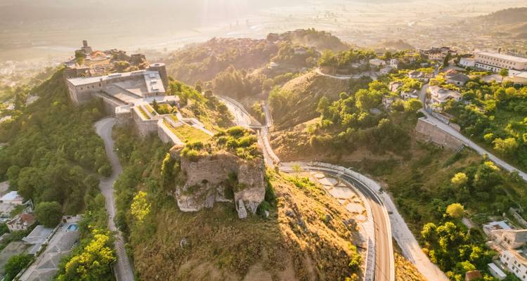 Zonnig luchtfoto van het Gjirokastra fort dat op een heuvel zit met het stadje en de vallei gehuld in ochtendnevel.