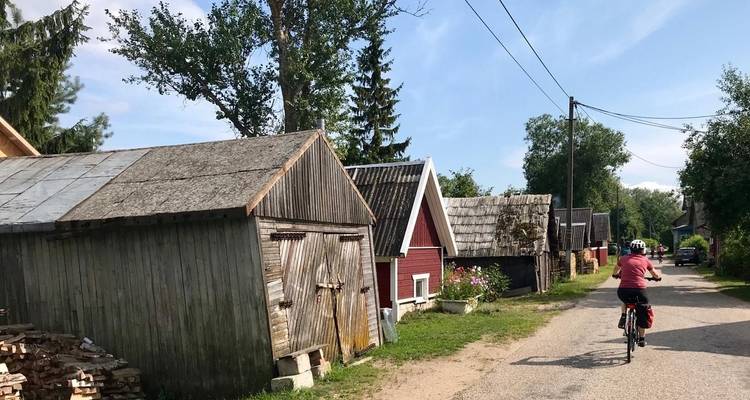 Personne faisant du vélo sur une route rurale avec des hangars en bois le long du chemin.