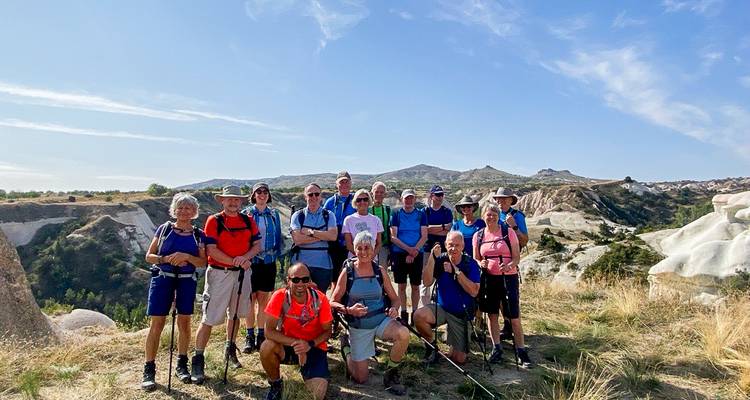 Grupo grande de senderismo posando juntos en una ladera capodocia soleada con formaciones de roca blanca detrás.