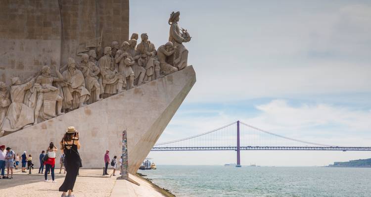 Monumento a los Descubrimientos lleno de estatuas junto al río Tajo con el Puente 25 de Abril de fondo y turistas tomando fotos.
