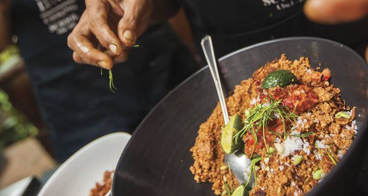 Primer plano de manos adornando un colorido plato balinés en una clase de cocina