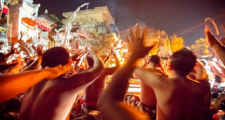 Actuación nocturna energética de danza Kecak con participantes levantando los brazos alrededor del fuego