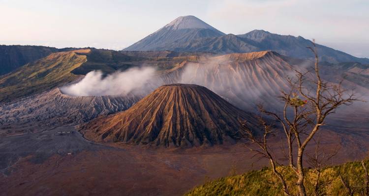 Paisaje volcánico dramático con el Monte Bromo humeante y picos distantes al amanecer