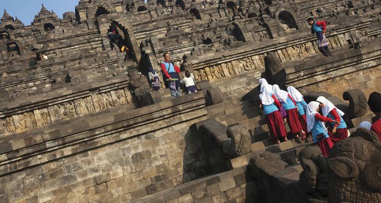 Visitantes, incluyendo niños de escuela, subiendo los empinados escalones de piedra del templo de Borobudur