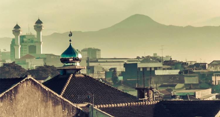 Paysage urbain avec dômes de mosquée et chaîne de montagnes lointaine sous une lumière matinale voilée.