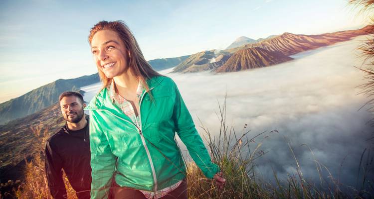 Des randonneurs souriants marchent le long d'une crête au-dessus d'une caldeira remplie de nuages et de pics volcaniques au lever du soleil.