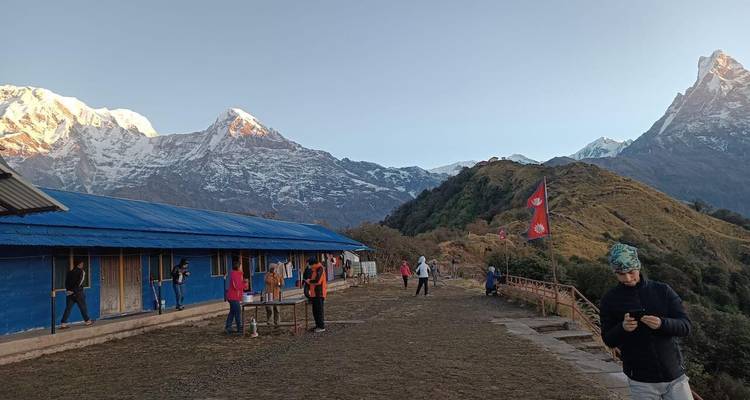 Los trekistas se reúnen cerca de un albergue de techo azul al amanecer con los nevados picos del Himalaya de fondo.