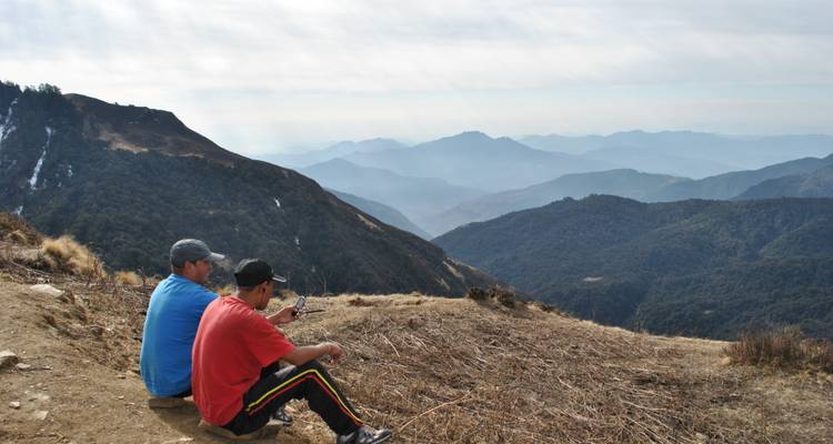 Dos trekkistas descansando en una cresta con vistas a capas de cadenas montañosas brumosas