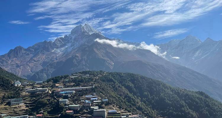 Mountain settlement of Namche Bazaar dotted with colorful houses beneath dramatic snow-clad peaks and wispy clouds.