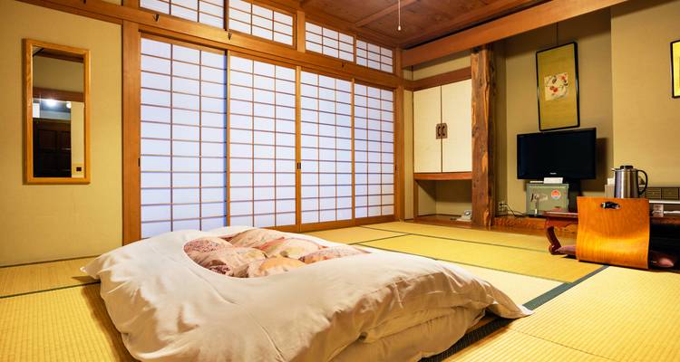 Traditionele Japanse tatami kamer met opgeouwen futon, shoji-schermen en houten balken.