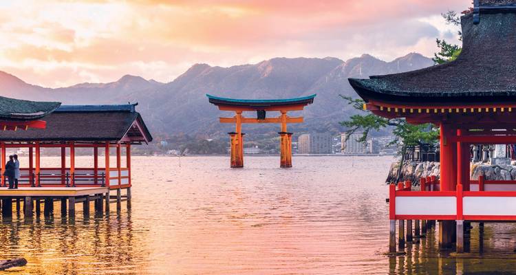 Het iconische zwevende torii-poortje van het Itsukushima Heiligdom gloedt bij zonsondergang, omlijst door paviljoens en bergen.
