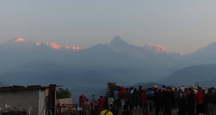 La multitud de la madrugada observa la primera luz rosada golpear los picos nevados del Himalaya sobre los valles brumosos.