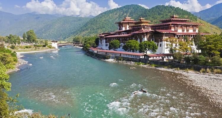 Colorful dzong by a river with a mountain backdrop.